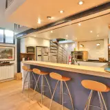 Un bar fait maison original avec des tabourets orange vif, une cuisine moderne et un escalier en colimaçon.