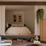 Chambre avec estrade, séparée par des rideaux blancs. Un lit douillet, des tableaux abstraits et une plante suspendue créent une atmosphère paisible.