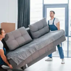 Deux déménageurs tentent de faire passer un canapé gris par une porte, mais la livraison du canapé ne passe pas la porte.