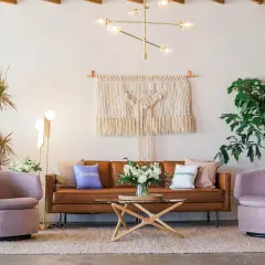 Salon moderne avec canapé en cuir marron, fauteuils roses poudrés et table basse en bois clair. Quelle couleur avec bois clair ? Le rose poudré et le marron s'harmonisent parfaitement.