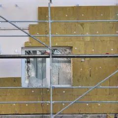 Échafaudage autour d'une maison en cours d'isolation avec de la laine de roche. Les panneaux isolants sont fixés sur le mur, prêts à isoler sa maison.