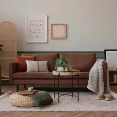Salon cosy avec un mur kaki, canapé marron, coussins, tapis, table basse en rotin et un buste antique.