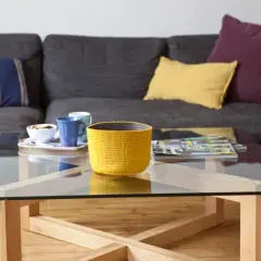 Table basse en verre et bois, avec un panier jaune, des tasses et des magazines. La hauteur de la table basse est idéale pour le canapé.