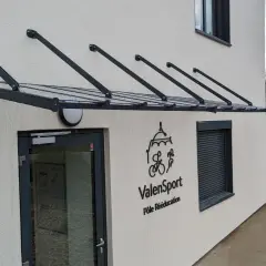 Une marquise moderne protège l'ouverture de la façade de cette maison, avec le logo ValenSport visible à côté de la porte.