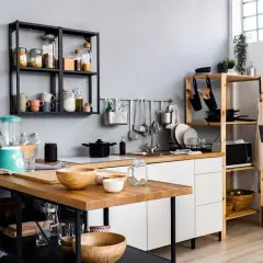 Une petite salle à manger moderne avec un îlot en bois, un mixeur turquoise et des étagères remplies d'ustensiles et d'épices.