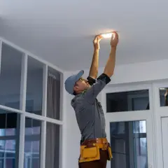 Un technicien installe un nouveau luminaire au plafond, un relamping définitif pour un éclairage moderne.