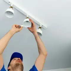 Un homme installe des spots LED sur un rail blanc. Le branchement en série ou parallèle de ces luminaires est en cours.