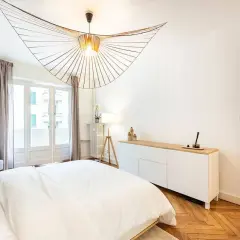 Un lustre design illumine cette chambre moderne. L'éclairage chambre est complété par une lampe sur trépied et une lumière douce émanant de la fenêtre.