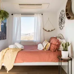 Une chambre d'amis cosy avec un lit orange, des coussins texturés, une couverture jaune et une vue désertique.