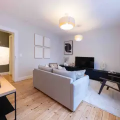 Salon moderne et lumineux, prêt à être habité. Le home staging met en valeur le canapé gris, le meuble TV noir et le parquet en bois.