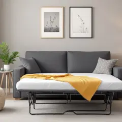 Un canapé-lit gris transformé en lit, prêt à accueillir des invités. Une couverture jaune apporte une touche de chaleur à cette chambre.