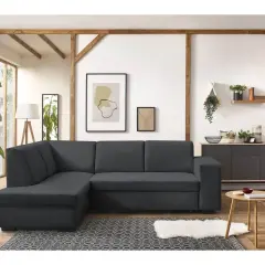 Un canapé d'angle gris foncé, parfait pour un salon feng shui, avec des poutres apparentes et des plantes vertes.