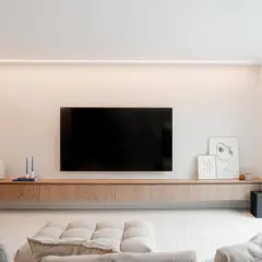 Un meuble TV suspendu, épuré et en bois, avec une télévision et des décorations. Idéal pour un salon moderne.