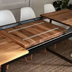 Détail du système de rallonge de table en bois, montrant les coulisses métalliques et les extensions empilées.