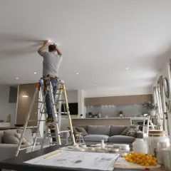Un homme installe des ampoules LED au plafond d'un salon moderne. La puissance de ces ampoules LED salon assure un éclairage optimal.