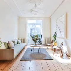 Un salon lumineux avec un canapé clair, des plantes et une grande fenêtre. Idéal pour savoir comment rendre une pièce plus lumineuse.