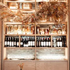 Éclairage cave à vin : étagères en bois remplies de bouteilles, bocaux et verres, le tout mis en valeur par une lumière douce et chaleureuse.