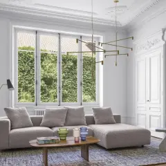 Salon moderne avec un grand canapé gris moelleux, une table basse en bois, un lustre doré et une cheminée ornée.