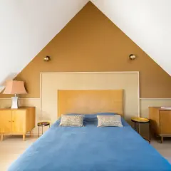 Chambre sous pente avec mur en **couleur ocre** et lit bleu. Meubles en bois vintage.