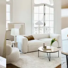 Un salon sans meuble TV, avec un canapé blanc, des lampes, des livres et une table basse en marbre.
