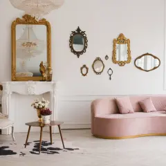Un salon élégant avec un canapé rose, une chaise vintage, une cheminée ornée et une collection de miroirs dorés. Une déco salon vintage moderne réussie.