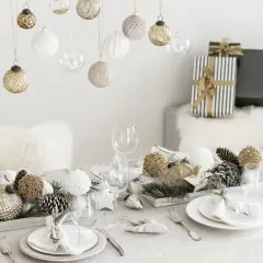 Une belle idée décoration table Noël : boules suspendues, centre de table naturel avec pommes de pin et ornements dorés, vaisselle élégante.