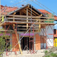 Une maison en pleine rénovation, avec échafaudages et matériaux de construction. Les propriétaires sont occupés à faire des travaux dans leur maison.