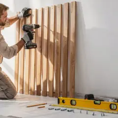 Un homme fixe des tasseaux en bois au mur avec une perceuse, une méthode astucieuse pour fixer des tasseaux au mur sans percer.
