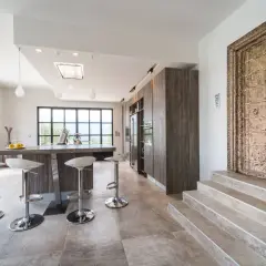 Cuisine moderne avec îlot central, tabourets chromés et une porte ancienne ornée. Un mélange audacieux de style Louis Philippe et contemporain.