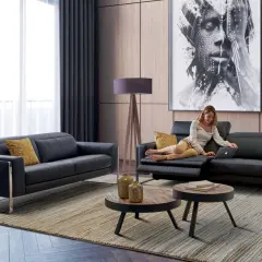 Salon moderne avec canapé noir, femme sur un fauteuil, tableau abstrait et tables basses.