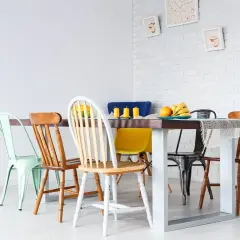 Un ensemble de chaises dépareillées entoure une table à manger. Des fruits et des bougies décorent la table.