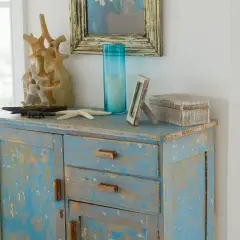 Meuble bleu délavé avec une patine bois effet vieilli, décoré d'objets marins et d'une boîte en bois.