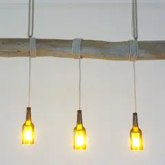 Lampe DIY originale : une branche flottée supporte trois bouteilles en verre ambré, transformées en luminaires.