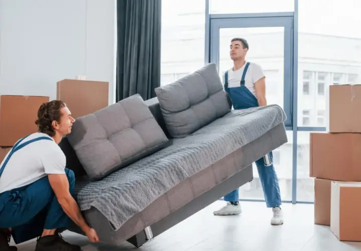 Deux déménageurs tentent de faire passer un canapé gris par une porte, mais la livraison du canapé ne passe pas la porte.