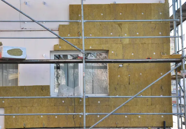 Échafaudage autour d'une maison en cours d'isolation avec de la laine de roche. Les panneaux isolants sont fixés sur le mur, prêts à isoler sa maison.
