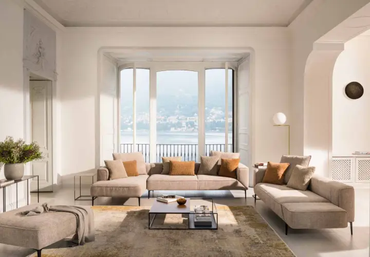 Un salon cocooning avec un canapé d'angle beige, des coussins douillets et une vue imprenable sur un lac.