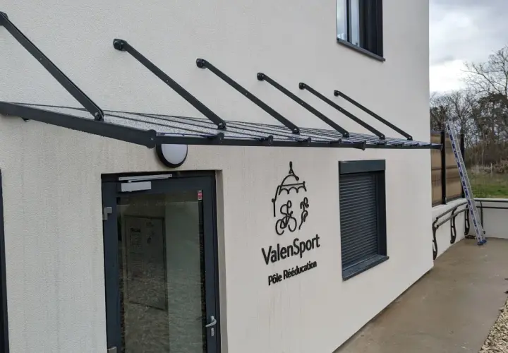 Une marquise moderne protège l'ouverture de la façade de cette maison, avec le logo ValenSport visible à côté de la porte.