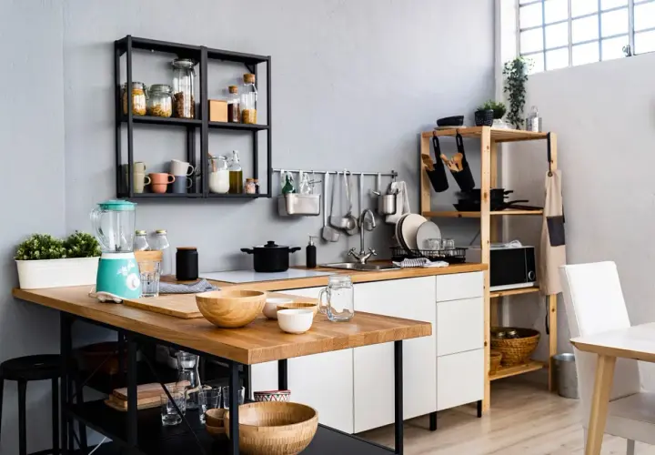 Une petite salle à manger moderne avec un îlot en bois, un mixeur turquoise et des étagères remplies d'ustensiles et d'épices.