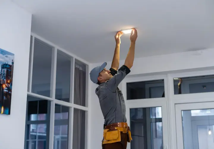 Un technicien installe un nouveau luminaire au plafond, un relamping définitif pour un éclairage moderne.