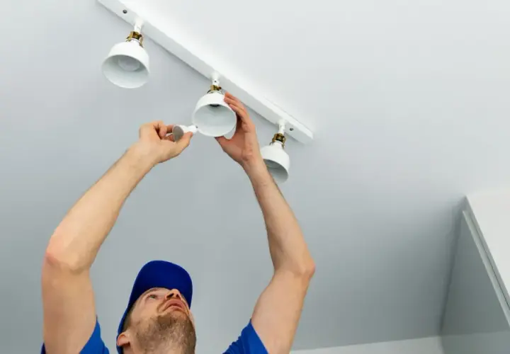 Un homme installe des spots LED sur un rail blanc. Le branchement en série ou parallèle de ces luminaires est en cours.