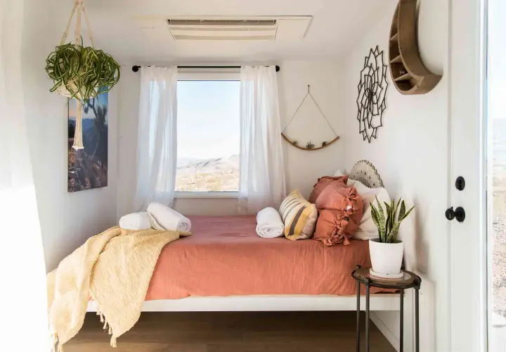 Une chambre d'amis cosy avec un lit orange, des coussins texturés, une couverture jaune et une vue désertique.