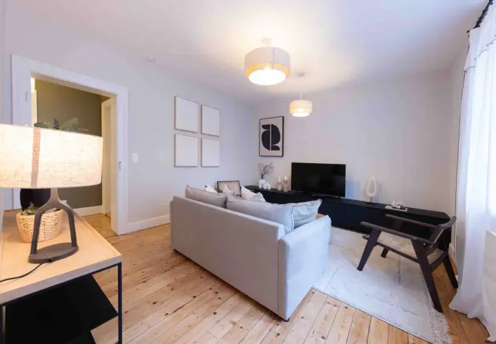 Salon moderne et lumineux, prêt à être habité. Le home staging met en valeur le canapé gris, le meuble TV noir et le parquet en bois.