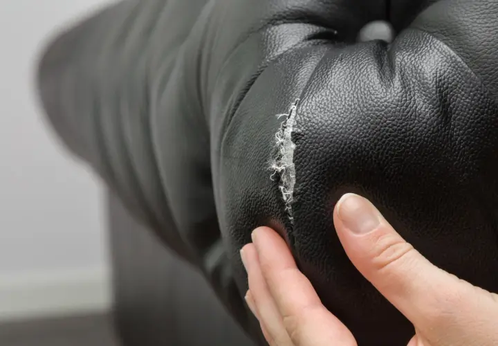 Un doigt touche une déchirure sur un canapé en cuir noir, montrant l'usure et affectant la durée de vie canapé.