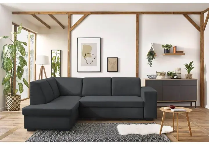 Un canapé d'angle gris foncé, parfait pour un salon feng shui, avec des poutres apparentes et des plantes vertes.