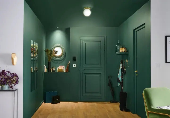 Une entrée chic et moderne avec des murs vert forêt, un miroir soleil, des sacs de shopping et une touche de plume de paon pour une deco entree élégante.