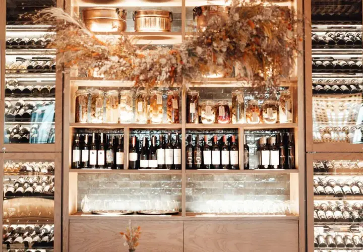 Éclairage cave à vin : étagères en bois remplies de bouteilles, bocaux et verres, le tout mis en valeur par une lumière douce et chaleureuse.