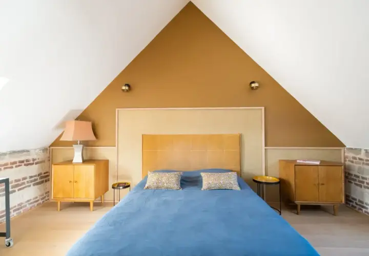 Chambre sous pente avec mur en **couleur ocre** et lit bleu. Meubles en bois vintage.