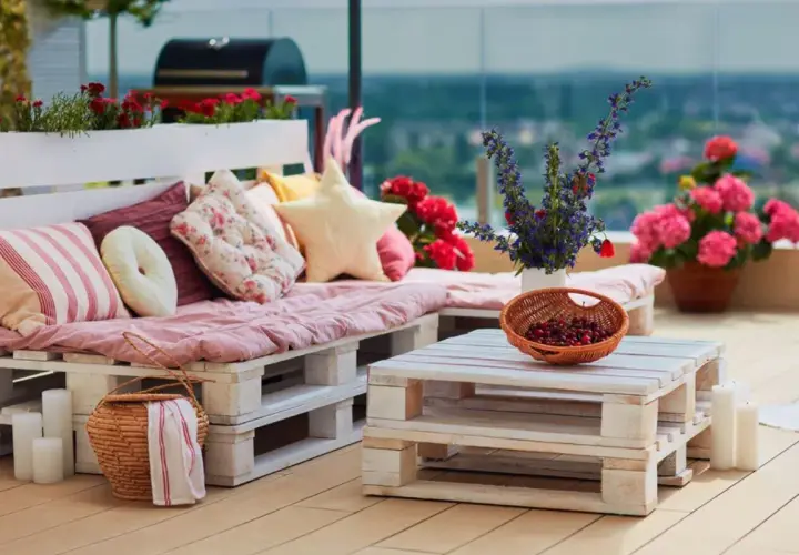 Un canapé en palette plan, confortable et coloré, orne cette terrasse avec des coussins douillets et des fleurs vives.