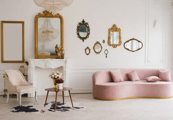 Un salon élégant avec un canapé rose, une chaise vintage, une cheminée ornée et une collection de miroirs dorés. Une déco salon vintage moderne réussie.
