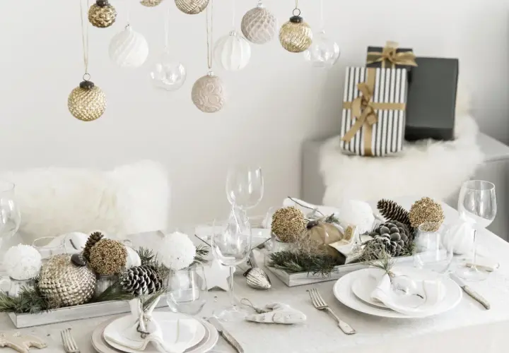 Une belle idée décoration table Noël : boules suspendues, centre de table naturel avec pommes de pin et ornements dorés, vaisselle élégante.